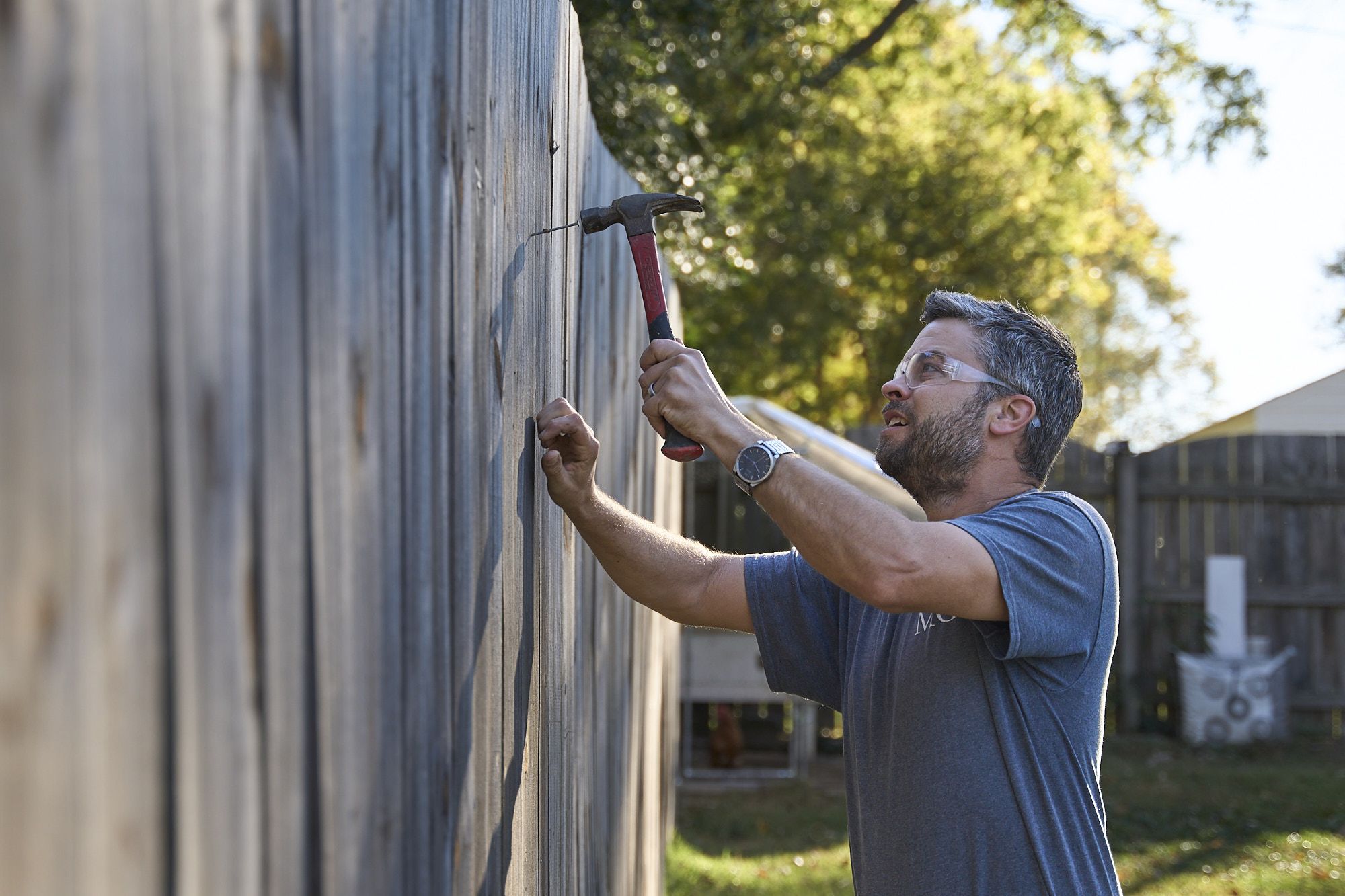 Contractor Hammering Nails Into Wooden Fence For Repair And Outdoor Maintenance